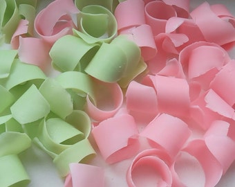 May include: Close-up of a pile of pastel-colored soap shavings. The shavings are in two colors: light green and pink. The shavings are curled and appear to be made of soap.