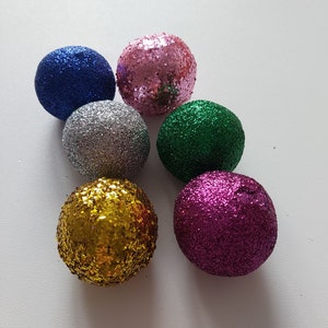 Könnte beinhalten: Sechs glitzernde Weihnachtskugeln in verschiedenen Farben, darunter rosa, blau, silber, grün, gold und lila.