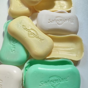May include: A close-up of several bars of soap, some are green, some are yellow, and some are white. All of the bars have the word "Safeguard" printed on them.