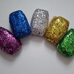 May include: Five small, glittery, decorative ornaments in a rainbow of colors: purple, blue, silver, gold, and green.