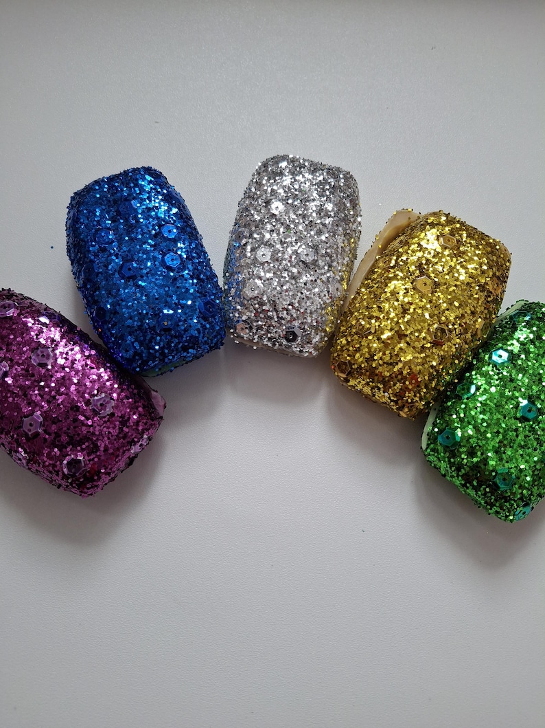 May include: Five small, glittery, decorative ornaments in a rainbow of colors: purple, blue, silver, gold, and green.