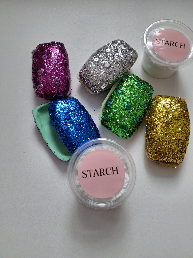 May include: Six small containers filled with glitter in various colors, including pink, silver, green, blue, and gold. Two containers of white powder labeled "STARCH" are also included.