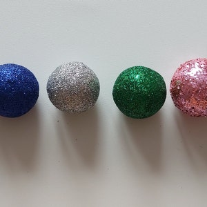 May include: Six small, round, glittery ornaments in different colors: gold, blue, silver, green, pink, and purple.