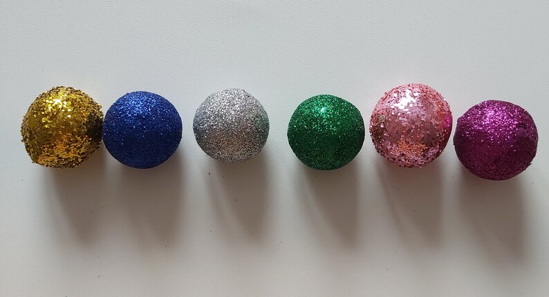 May include: Six small, round, glittery ornaments in different colors: gold, blue, silver, green, pink, and purple.