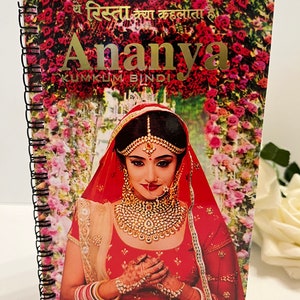 May include: A spiral bound notebook with a red, white and gold design. The cover features a woman in a red and gold bridal outfit with a red veil. The text on the cover reads "Ye Rista Kya Kehlata Hai Ananya Kumkum Bindi".