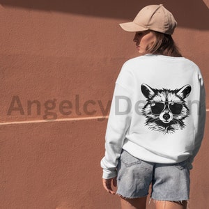 K&ouml;nnte beinhalten: Wei&szlig;es Sweatshirt mit einer schwarz-wei&szlig;en Illustration eines Waschb&auml;ren mit Sonnenbrille auf der R&uuml;ckseite. Der Waschb&auml;r schaut mit einem ernsten Ausdruck nach vorne.