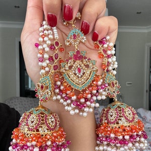 May include: A pair of gold-tone earrings featuring pink, orange, and turquoise beads. The earrings have a large, ornate design with a floral motif and are embellished with clear crystals.