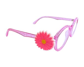 May include: Pink eyeglasses with a glittery finish and a large pink daisy flower accent on the left side. The daisy has a yellow center and white petals. The frames are a light pink color.