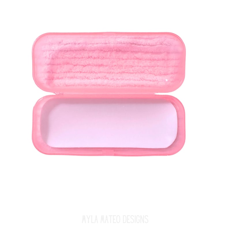 May include: A rectangular pink plastic case with a hinged lid. The interior of the lid features a textured pink lining, while the bottom section of the case has a smooth, light pink base. The text MYLA MATEO DESIGNS is printed at the bottom.