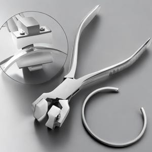 May include: A silver-colored bracelet bending tool with a matching bracelet on a gray surface. The tool has long handles and a detailed close-up view of the tool's mechanism. The bracelet is a simple, open-ended design.
