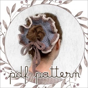Op de afbeelding: Een gehaakte haaraccessoire in blauw, bruin en crème, met een gerimpelde rand en een strik. De tekst "pdf pattern" is zichtbaar. Het accessoire wordt op de achterkant van het hoofd van een persoon gedragen. Het ontwerp is bloemig.