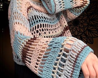 Op de afbeelding: Een pastelkleurige, open geweven gehaakte top. De top heeft een mix van lichtblauw, roze, grijs en bruin garen. De mouwen zijn lang en uitlopend. Het haakontwerp creëert een netachtig patroon.