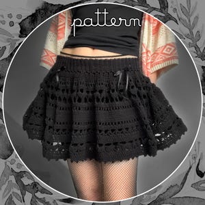 May include: A black, flared crochet skirt with detailed openwork and ribbon embellishments. The word "pattern" is written in cursive. The skirt is worn with a black top and fishnet stockings. The skirt's design is visible.