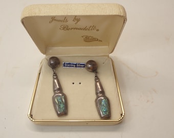 May include: Vintage sterling silver earrings in a cream-colored jewelry box. The earrings have a round top and a bottle-shaped pendant with abalone shell inlay. The box is labeled "Jewels by Bernadette" and "Sterling Silver".