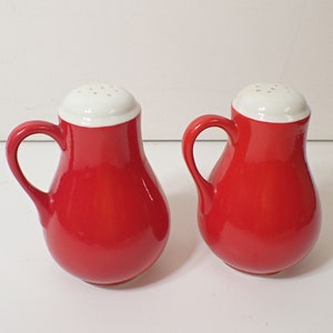 May include: A set of two red ceramic salt and pepper shakers with white lids and handles.