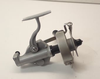 May include: A silver-colored fishing reel with a curved handle and a black spool. The reel has a metal frame and a handle for winding the line. The reel is designed for use in freshwater or saltwater fishing.