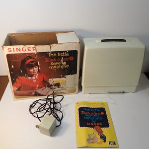 May include: A white Singer Touch & Sew sewing machine with its original box, instruction manual, and power cord. The box features a young girl using the machine and the text "The little Touch & Sew sewing machine". The instruction manual has the same text and a picture of a girl using the machine.