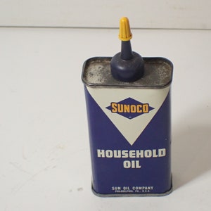 May include: A blue and white metal can with a yellow and black Sunoco logo. The can is labelled "Household Oil" and has a blue oiler with a yellow cap on top.