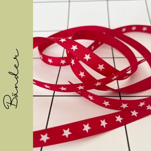 Könnte beinhalten: Rotes Band mit weißen Sternen bedruckt. Das Band ist gekräuselt und verdreht.