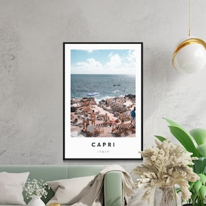 Puede incluir: Una fotografía de una escena de playa en Capri, Italia. La foto muestra una playa rocosa con gente relajándose en tumbonas bajo sombrillas. El mar es azul y el cielo está despejado.