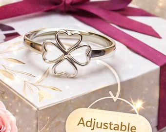 Op de afbeelding: Een zilveren ring met een klaverbladontwerp bestaande uit vier hartvormige contouren. De ring ligt op een witte geschenkdoos met een donkerroze lint en een roze roos. De tekst bevat Handmade, 925 Silver, Gift Ready, Adjustable Fit en Perfect Gift.