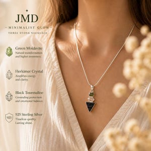 Puede incluir: Un collar de tres piedras con una moldavita verde, un cristal Herkimer transparente y un colgante triangular de turmalina negra en una cadena de plata. El texto incluye JMD, Minimalist Glow, Three Stone Necklace y descripciones de las piedras.
