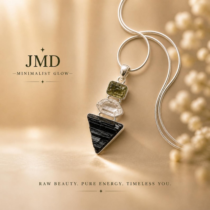 Puede incluir: Un collar de plata con un colgante de tres piedras apiladas: una piedra rectangular de color verde oliva, una piedra hexagonal transparente y una piedra triangular negra. El texto JMD MINIMALIST GLOW y RAW BEAUTY. PURE ENERGY. TIMELESS YOU. es visible.