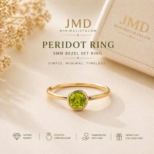 May include: A gold-toned ring featuring a round, 5mm bezel-set green peridot gemstone. The text on the image reads JMD MINIMALISTGLOW, PERIDOT RING, 5MM BEZEL SET RING, SIMPLE. MINIMAL. TIMELESS., NATURAL PERIDOT, SOLID 925 STERLING SILVER, HANDCRAFTED WITH CARE.
