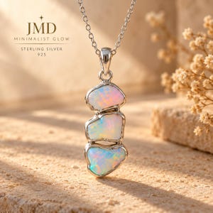 May include: A sterling silver 925 necklace featuring a vertical pendant with three irregular, iridescent opal stones set in metal. The text JMD MINIMALIST GLOW STERLING SILVER 925 is visible in the upper left corner of the image.