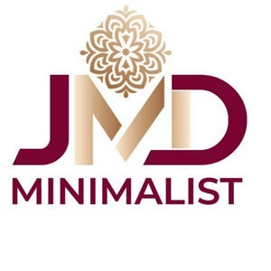 Puede incluir: Un logotipo que presenta las letras JMD en un esquema de color degradado granate y dorado. Sobre la letra M hay un icono de mandala floral dorado. Debajo de las letras JMD, la palabra MINIMALIST est&aacute; impresa en letras may&uacute;sculas granates.