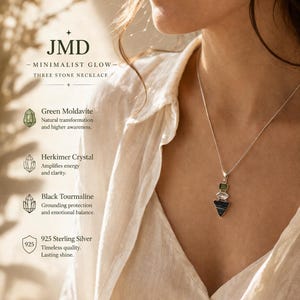 Puede incluir: Un collar de plata con tres piedras apiladas verticalmente: una peque&ntilde;a moldavita verde, un cristal de Herkimer transparente y una turmalina negra triangular m&aacute;s grande. El colgante cuelga de una fina cadena de plata con texto visible.