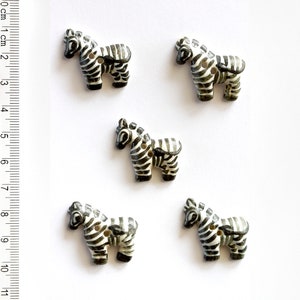 May include: Five black and white zebra buttons. The buttons are made of plastic and have a flat back. They are about 1 inch in size.