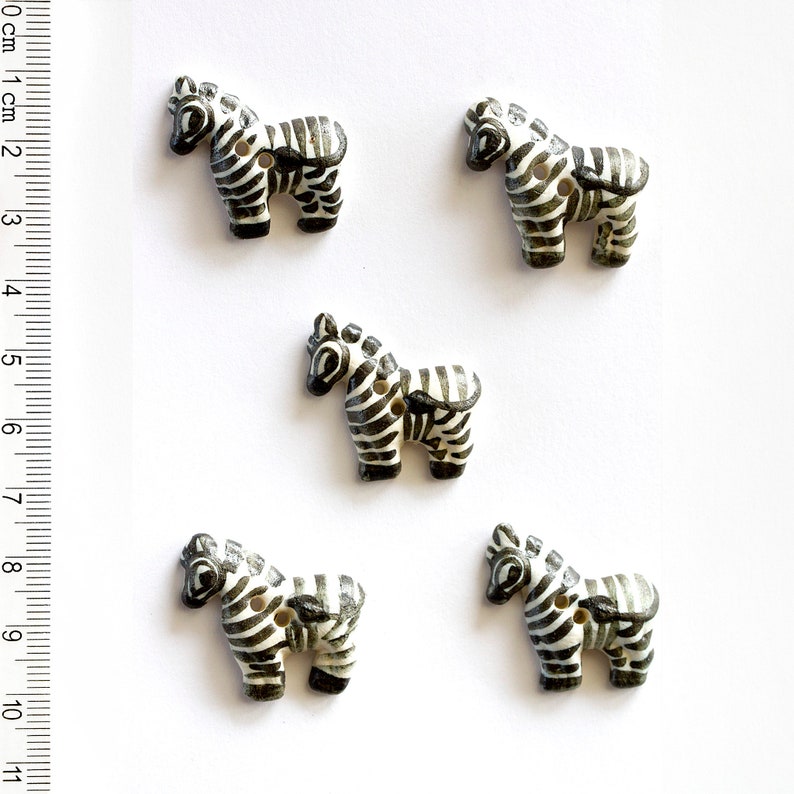 May include: Five black and white zebra buttons. The buttons are made of plastic and have a flat back. They are about 1 inch in size.