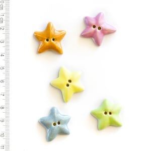May include: Five ceramic star-shaped buttons in different colors: yellow, light blue, light green, orange, and pink. The buttons have two holes each.