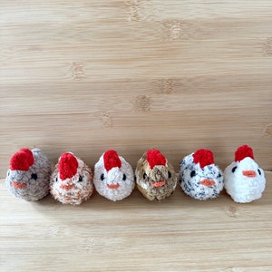 May include: Six small crocheted chicks in different colors and patterns, lined up on a wooden surface.
