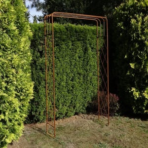 May include: A tall, rectangular garden arch made of thin, rusted metal rods. The structure features a flat top and side panels with a simple diamond-shaped lattice pattern. The arch stands upright, providing a frame for outdoor garden pathways.