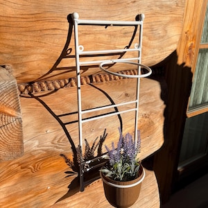 Może przedstawiać: Biały metalowy wieszak na ręczniki na ścianę z małym, okrągłym uchwytem i brązową doniczką z lawendą. Wieszak jest zamontowany na drewnianej ścianie. Doniczka ma białą obwódkę, a lawenda fioletowe kwiaty.