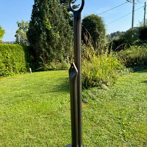 Puede incluir: Estaca de jard&iacute;n de metal negro con un anillo en la parte superior. La estaca est&aacute; dise&ntilde;ada para ser insertada en el suelo.