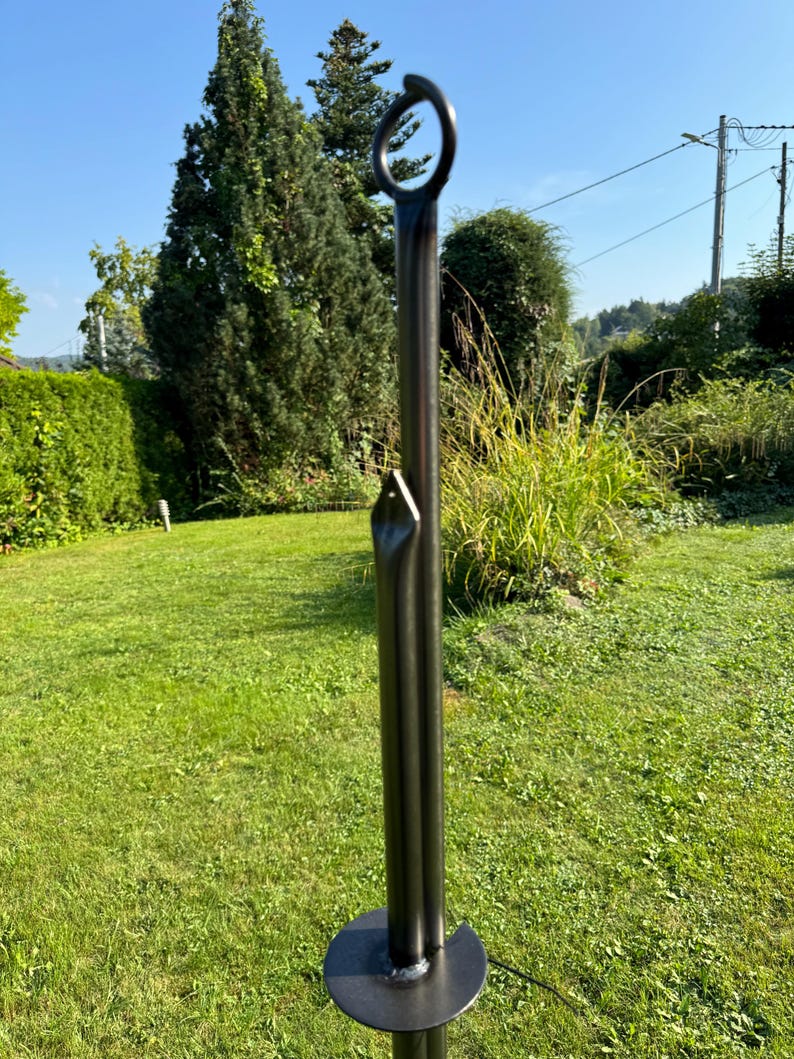 Puede incluir: Estaca de jard&iacute;n de metal negro con un anillo en la parte superior. La estaca est&aacute; dise&ntilde;ada para ser insertada en el suelo.