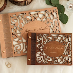 Peut inclure: Deux albums photo en bois avec des motifs floraux complexes et des découpes. Les albums sont personnalisés avec les noms "Jasper & Amelia" et la date "09.09.2024".