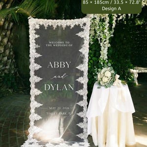 Puede incluir: Un letrero de bienvenida de boda rectangular con un panel de tela blanca transparente y bordes de encaje intrincados. El texto dice: WELCOME TO THE WEDDING OF ABBY and DYLAN MAY 23, 2026 TINLEY PARK, IL. El letrero mide 85 x 185 cm.
