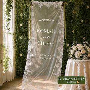 以下が含まれることがあります： 75 x 200cmの白いレースの長方形のウェディングサイン。「WELCOME TO THE WEDDING OF ROMAN and CHLOE JULY 06, 2025 FRANKLIN, TN」という文字が記されています。透け感のある生地は、上部の角にあるオリーブグリーンのリボンで吊るされています。