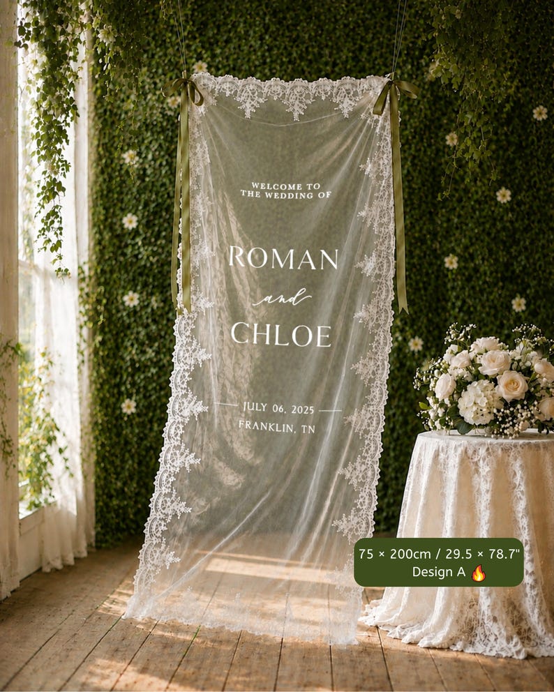 以下が含まれることがあります： 75 x 200cmの白いレースの長方形のウェディングサイン。「WELCOME TO THE WEDDING OF ROMAN and CHLOE JULY 06, 2025 FRANKLIN, TN」という文字が記されています。透け感のある生地は、上部の角にあるオリーブグリーンのリボンで吊るされています。