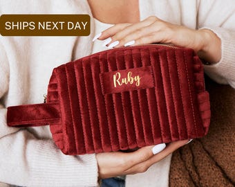 Op de afbeelding: Een bordeauxrode, gewatteerde toilettas van fluweel met een gouden rits en een gouden label met de tekst "Ruby".