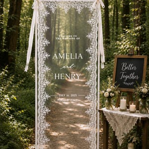 Puede incluir: Un letrero de bienvenida para bodas rectangular de 75 por 200 cm, con un panel transparente enmarcado en blanco y adornado con encaje blanco. El texto dice: WELCOME TO THE WEDDING OF AMELIA and HENRY JULY 16, 2025 PUGLIA, ITALY. Dise&ntilde;o A.