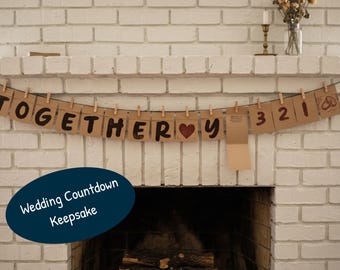 May include: A horizontal banner made of brown paper cards clipped to a black string. The cards feature the black text TOGETHER, a red heart symbol, the letter Y, and the numbers 3, 2, 1, followed by a small illustration of two wedding rings.