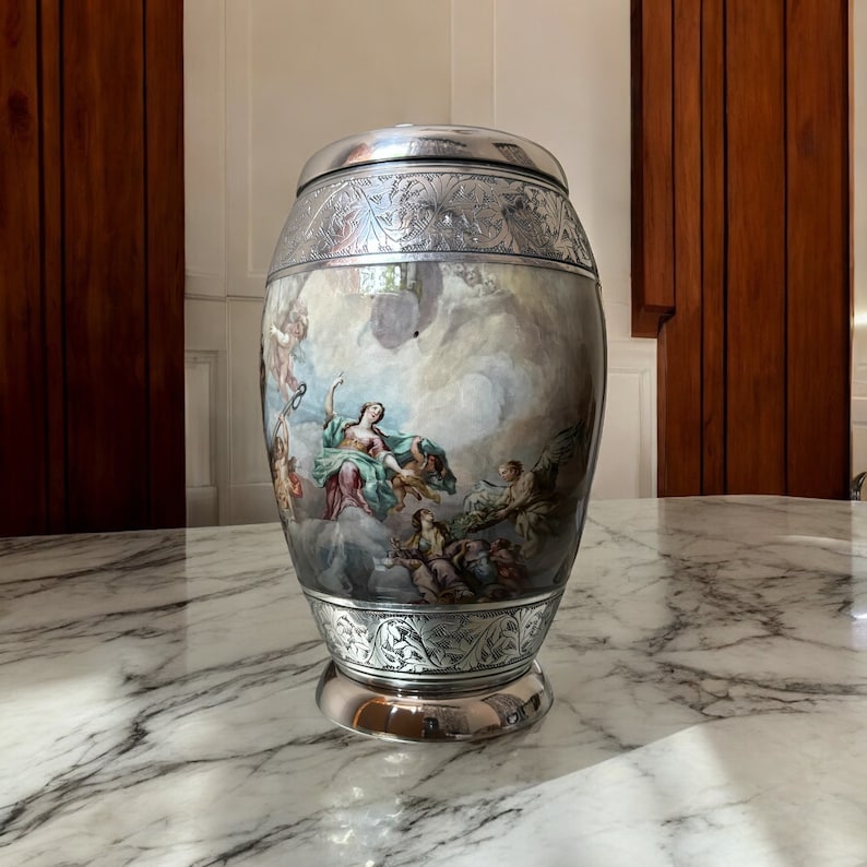 May include: A silver urn with an ornate design and a painted scene of a woman and angels in the clouds.