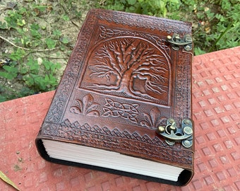 May include: A brown leather journal with a tree of life design embossed on the cover. The journal has two brass clasps to keep it closed.