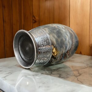 May include: A silver and gray ceramic urn with a floral design and a cloudy sky scene. The urn has a round base and a wide opening.