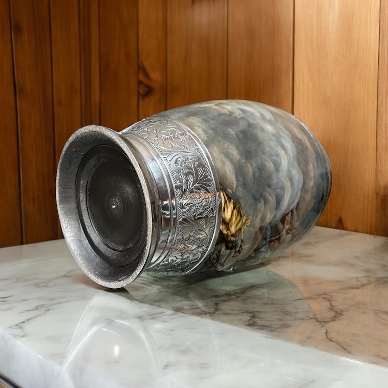 May include: A silver and gray ceramic urn with a floral design and a cloudy sky scene. The urn has a round base and a wide opening.